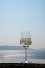 A wine glass with ice cubes stands on a balcony railing with a blue sky