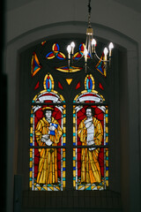 stained glass window with two men in yellow clothes and a blue book. The window is illuminated by a...