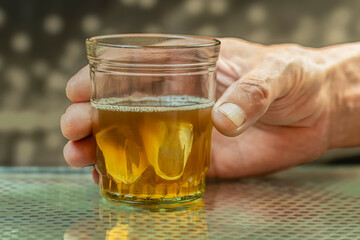 Glass of whiskey and ice cubes on a blurred background. Man's hand holding a glass.