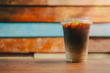 Ice coffee in cafe. Iced Coffee Drink in Clear Plastic Cup Against Rustic Wooden Background with Warm Natural Lighting