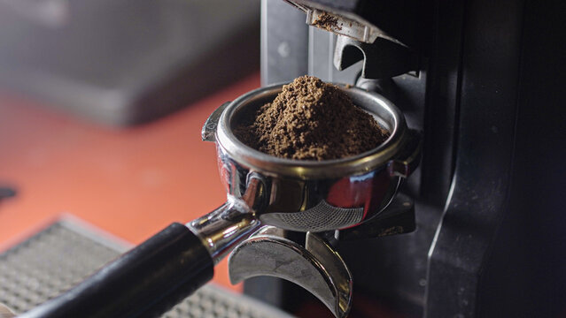 Coffee grinder grinds fresh coffee beans into a portafilter. Barista grind espresso coffee bean with grinder machine. Ambient light. Selective focus - Powered by Adobe