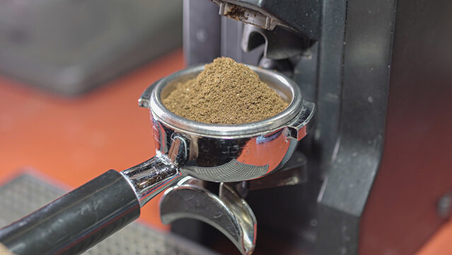 Coffee grinder grinds fresh coffee beans into a portafilter. Barista grind espresso coffee bean with grinder machine. Ambient light. Selective focus - Powered by Adobe