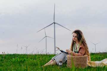 Eco-conscious woman writing in notebook near wind turbines