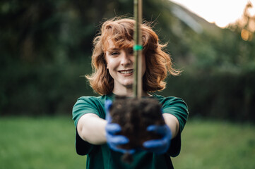 Young woman holding a small tree sapling wearing gloves