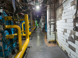 A long passageway in a boiler room with massive gas boilers and intricate pipework creates an impressive perspective.