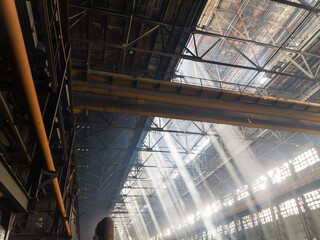 A powerful overhead crane dominates the grimy workshop, where sunbeams piercing through skylight windows