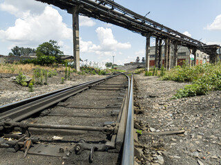 Railway tracks disappearing under the shadow of a massive pipeline overpass create a powerful image of industrial infrastructure.
