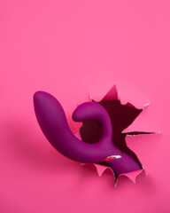 Raspberry sex toy sticks out of pink paper background. Vertical photo. Copy space. 