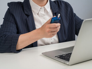 Business woman smoking an electronic cigarette while working on a laptop. Tobacco heating system.
