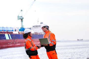 Two port engineers in high-visibility orange uniforms and hard hats communicate while inspecting...