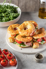 Homemade bagle sandwiches with ham, soft cheese and vegetables on whire board on kitchen table background. Homemade burgers