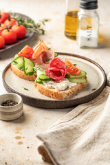 Delicious sandwiches with cream cheese, salami, cucumber, tomatoes on a plate on light background. Homemade breakfast