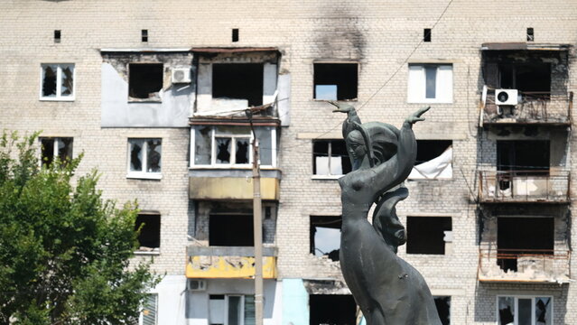 Monument of a woman in Russian national dress against the backdrop of a multi-story building destroyed by the russians. Izum, Ukraine.11.08.2024