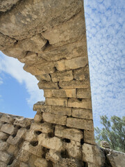 Weathered stone arch viewed from below against a bright blue sky with scattered clouds, capturing...