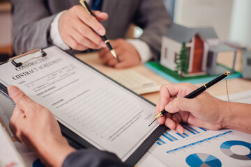 Real estate agent discusses and explains the steps of buying and selling a home. After that, they sign the sales contract in the office with a model home, laptop, calculator, documents, charts on the 