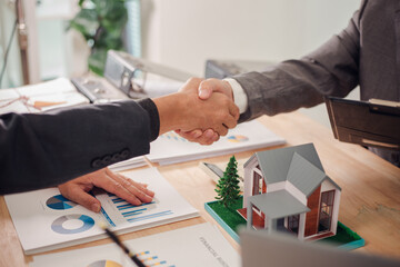 Real estate agent shaking hands with client after signing sales contract in office with house...