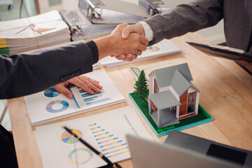 Real estate agent shaking hands with client after signing sales contract in office with house...