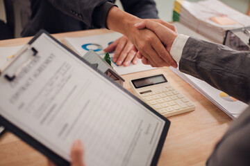 Real estate agent shaking hands with client after signing sales contract in office with house...