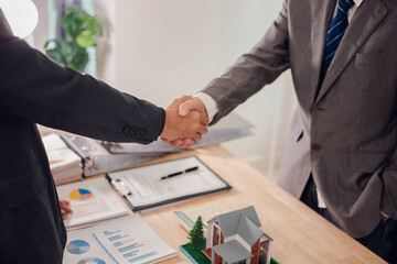 Real estate agent shaking hands with client after signing sales contract in office with house...