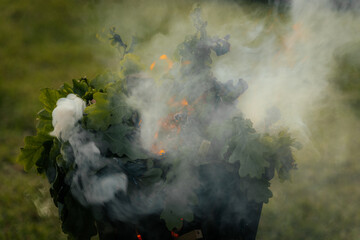 A metal fire basket with tall, bright orange flames burns on a grassy lawn, with embers rising into...