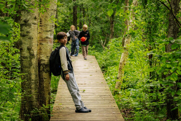 Children exploring a lush green forest, walking and leaning on a wooden boardwalk path surrounded by trees and foliage in a peaceful natural setting.