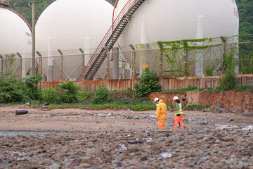 Two environmental specialists in safety gear conduct a field investigation at a polluted coastal site, collecting data and assessing contamination risks near an industrial zone.