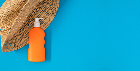 Sun hat and orange bottle of sunscreen on blue background. Flat lay.