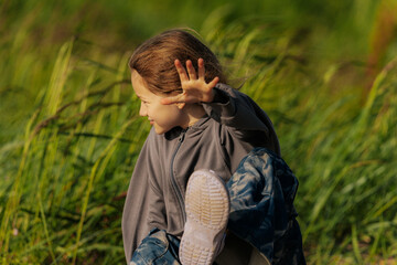 A smiling girl sits on a weathered log in a grassy field, wearing star-patterned pants and a gray...