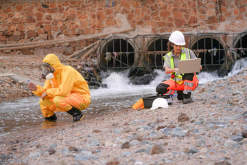 Environmental field team in protective gear analyzes water samples on a polluted beach. One holds a...