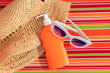 Summer beach concept. Stylish sunglasses, hat and sunscreen in an orange bottle lie on a striped chaise lounge. Top view.