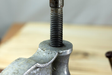 Close-up of a metal clamp with a threaded bolt and drill bit. The clamp is positioned on a wooden...