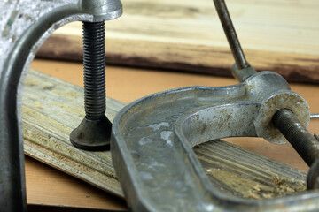 A metal clamp is securing two wooden pieces together on a workbench. The clamp features a threaded...