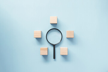 Magnifying glass surround by empty wooden block on pastel blue background. Business concept on business target, strategy development, search for idea and focus.