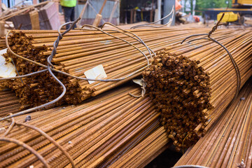 Stacked steel rods are prominently observed at a bustling construction site in progress