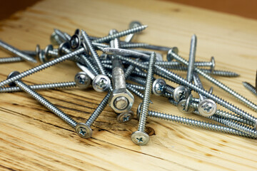 A collection of metal screws scattered on a wooden surface. The screws vary in size and design,...