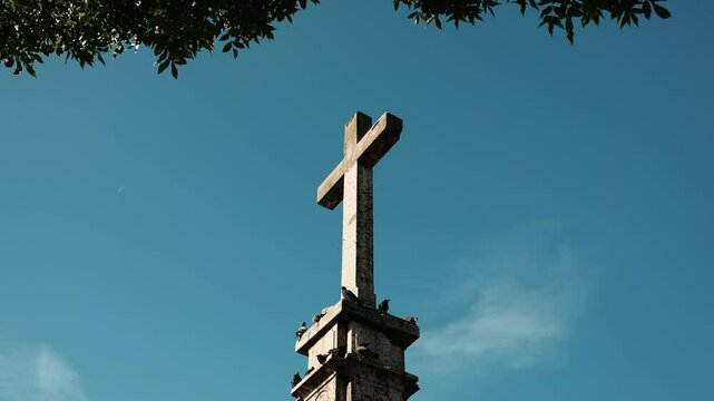 Stone cross monument with pigeons perched on it under a deep blue sky in Vrsac, Serbia. Religious symbol and historical landmark. 4k horizontal footage