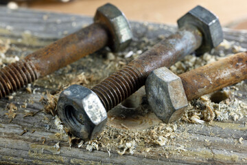 Close-up of rusty bolts and nuts on a wooden surface. Shavings and drill marks are visible,...