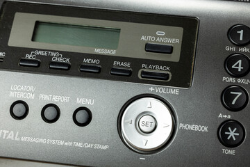 A close-up of a retro telephone with an answering machine. The device features buttons for volume,...