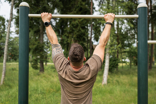 A man does pull-ups on a horizontal bar at a sports ground in the park. Outdoor workout and the concept of a healthy lifestyle and strength.