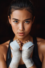 Vertical young confident Asian female Muay Thai boxer wrapping hands with sports bandage preparing to fight