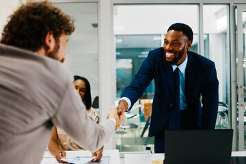 Two businessmen shaking hands over a desk in a modern office