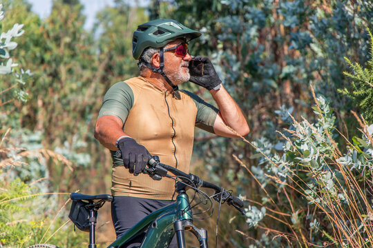 Senior cyclist wearing helmet and gloves using smartphone on electric mountain bike