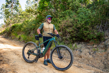 Senior cyclist taking a break on his electric mountain bike on a forest trail