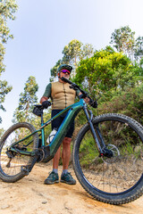 Senior cyclist taking a break with his electric mountain bike in a forest