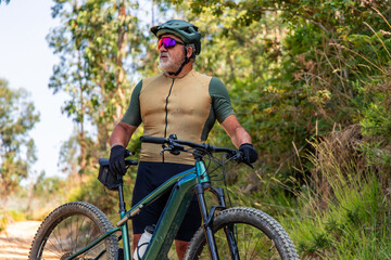 Senior cyclist taking a break with his electric mountain bike in the woods