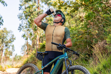 Senior cyclist drinking water on electric mountain bike in forest