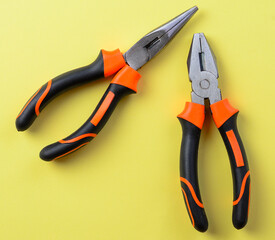 Flatnose and longnose pliers arranged on yellow background for repair and DIY theme