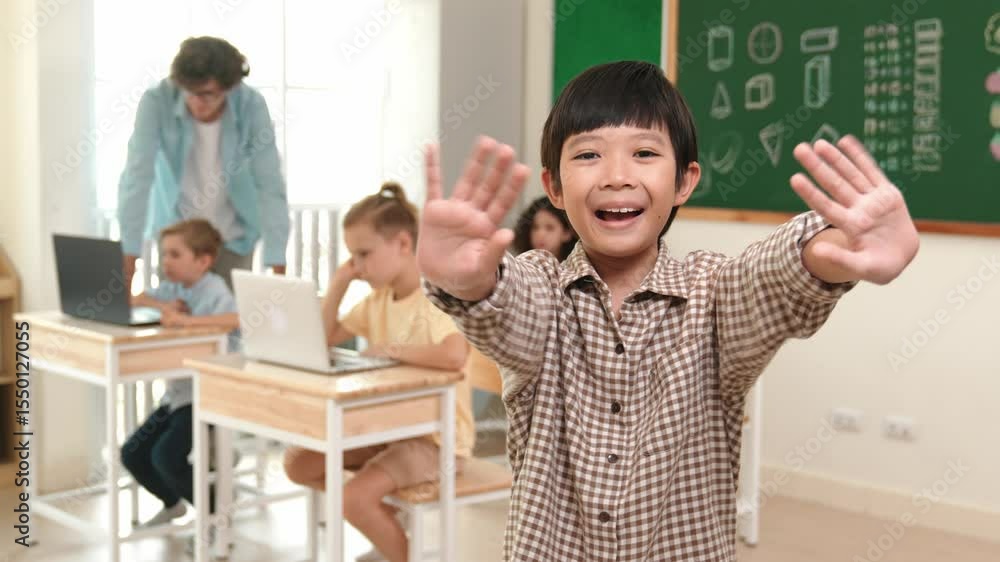 Poster asian boy looking at camera while waving hands and standing at blackboard. skilled child greeting wh