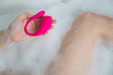 A woman lies in a bubble bath and holds a curved pink vibrator.