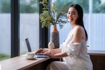 Asian freelance people business female talking making using casual working with laptop computer and coffee at home in the living room indoors artificial rose bouquet of red and pink roses rose vase